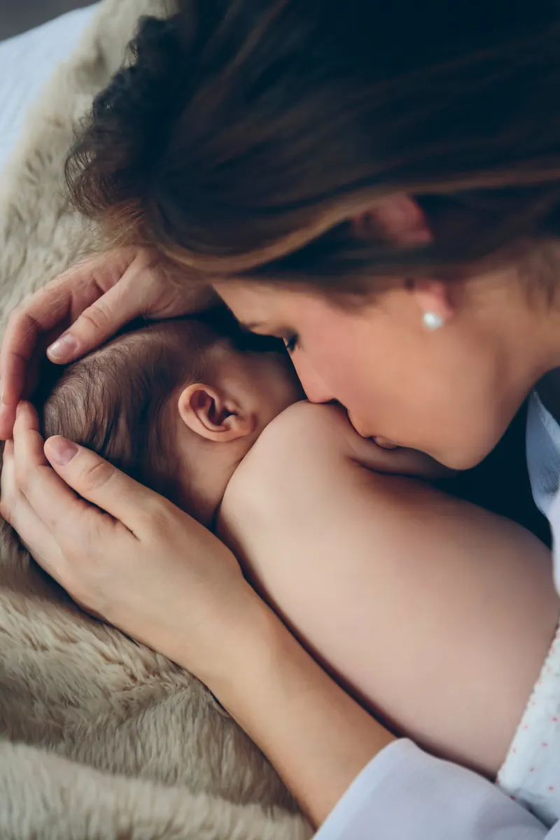 A mother leaning over her newborn baby, who is lying on a bed